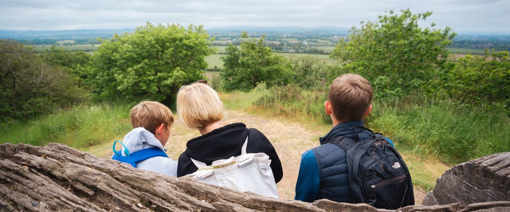 A family sitting on a bench looking at a view on top of a hill