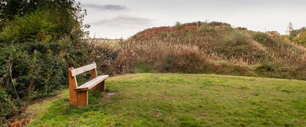 A wooden bench on a grassy clearing with hills behind.