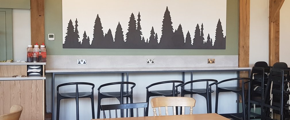 Interior of the cafe at High Lodge, showing tables, chairs and a wall mural of tree silhouettes