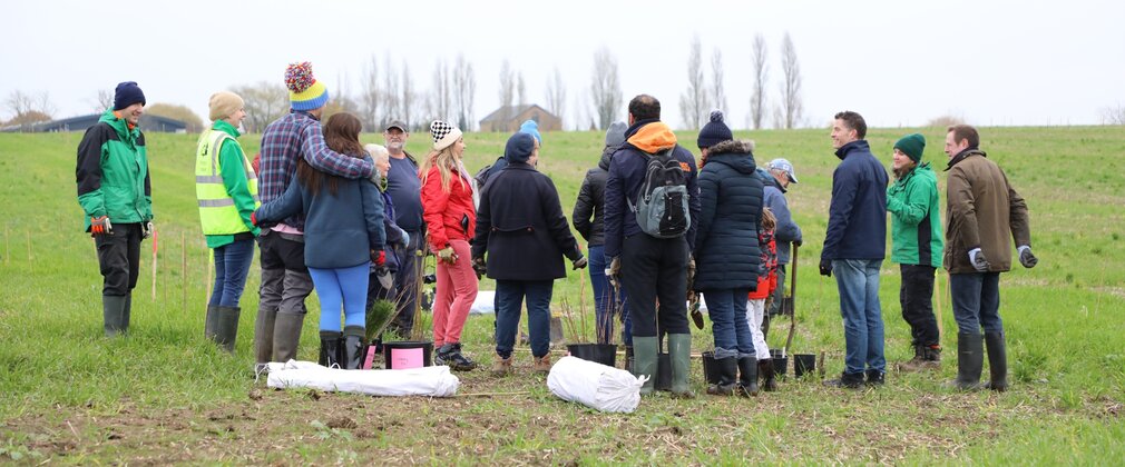 A small crowd of people wearing warm outdoor clothing stand in a group with tree planting equipment