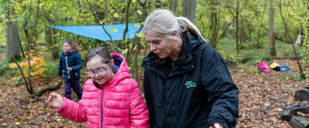 Girl in a pink coat in the woods talking to a forest school teacher
