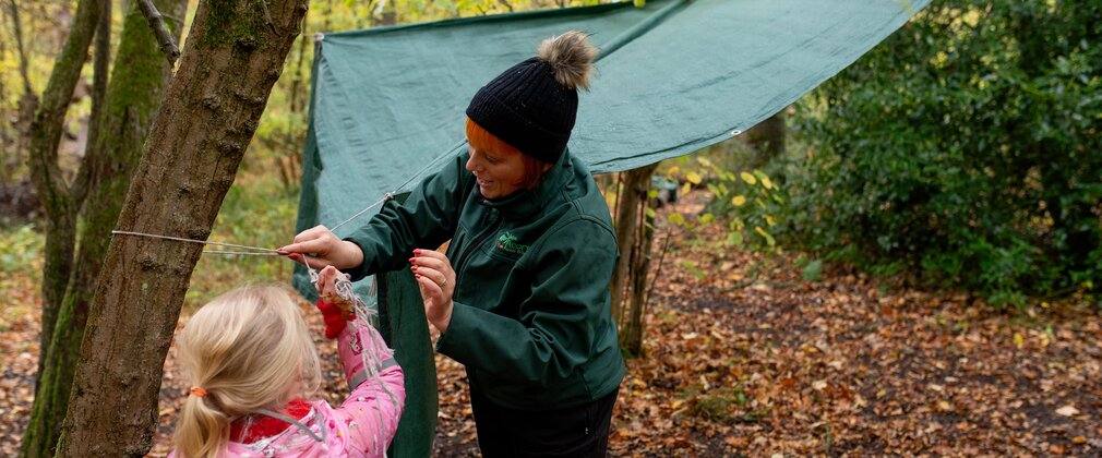 Girl putting up a shelter in the woods.