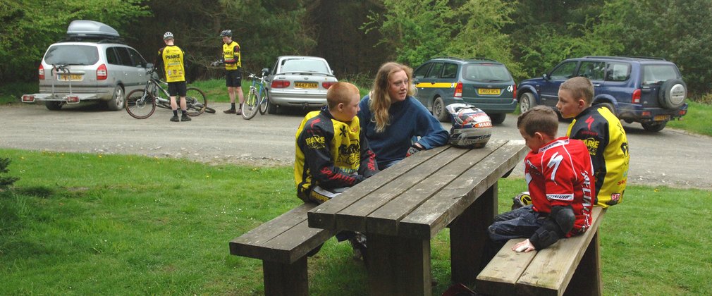 People wearing mountain biking gear are sat at a picnic table at Hopton Wood