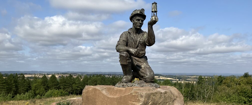 A sculpture of a miner holding a lamp, on top of the hill at Silverhill Wood