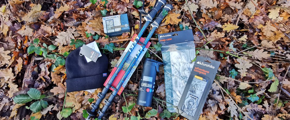 Hat, binoculars, walking poles, water bottle, map case and a compass on the forest floor