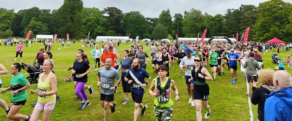 A group of runners at a start line on grassy terrain with trees lining the background.