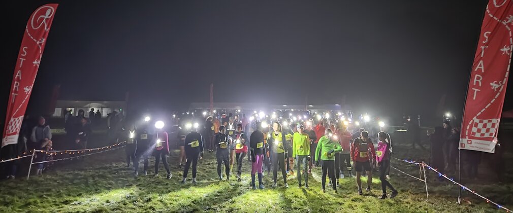 A group of runners on a night run at the start line in bright coloured clothing and flashlights.