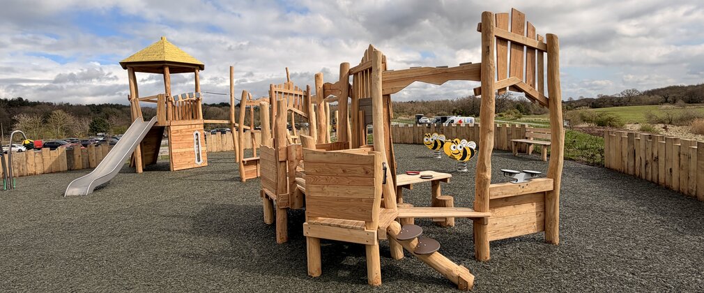 A number of wooden play structures in the shape of hillfort buildings on a flat surfaced playground