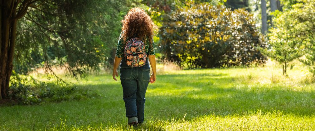 Woman walking on sunny day surrounded by the bright green forest