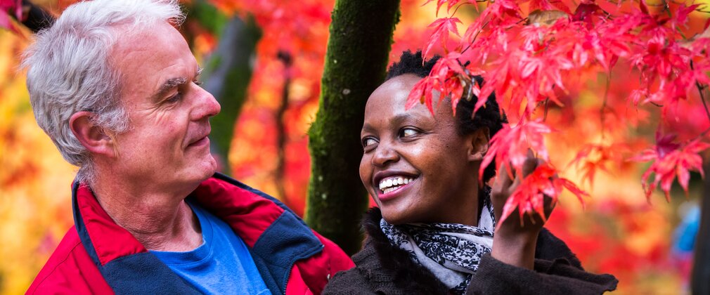 A man and woman smile at each other looking at a red maple tree