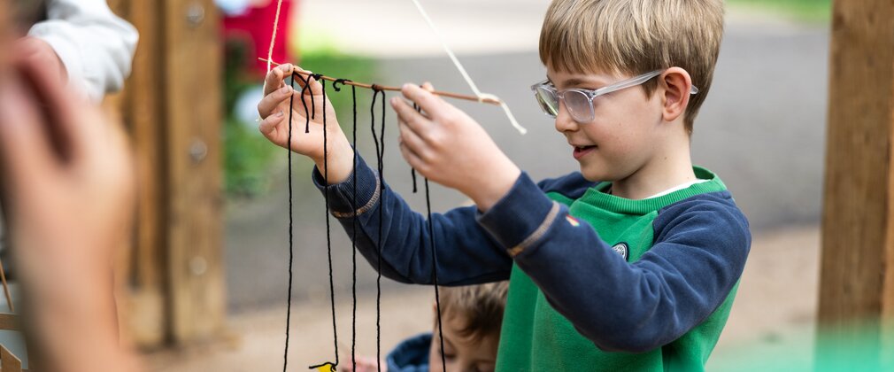 Young boy holding up a stick he has tied string to to create a mobile