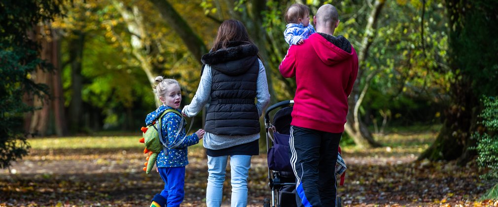 A family walk away from the camera with a baby in the fathers arms and a young boy looking behind him with mum holding the reins.