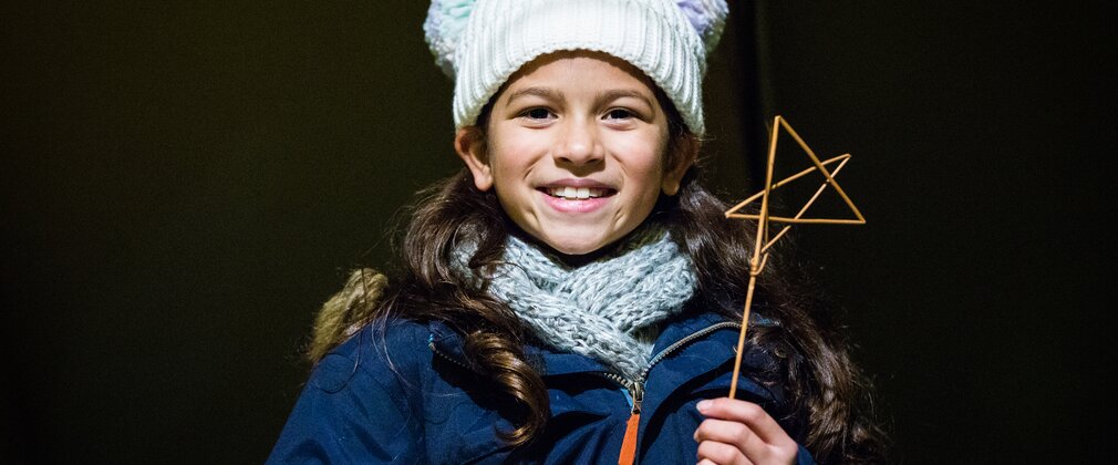 A young girl holds up a wooden stick star that she has created 