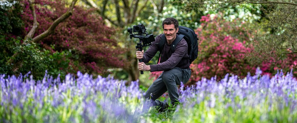 A camera man in a spring outdoor setting gets ready to film