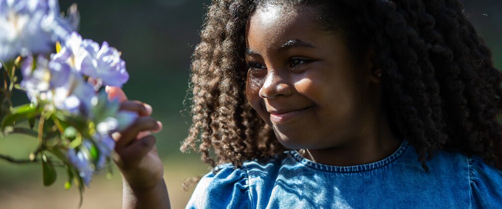 A little girl reaching out to take a closer look at flowers on a tree