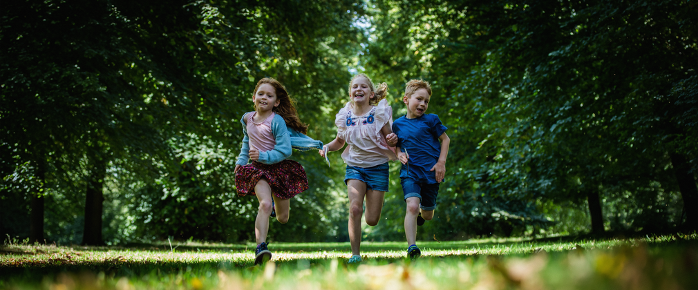 3 children run towards the camera in a woodland setting laughing.