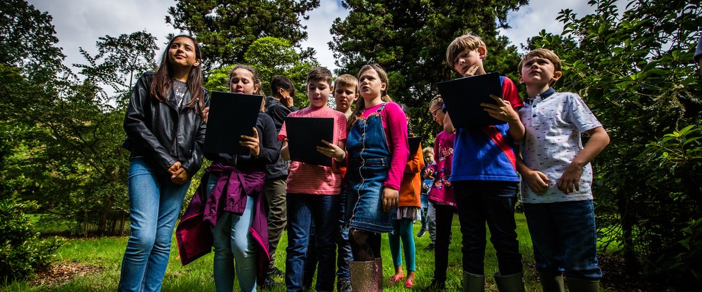 A group of children stand in a bunch with clipboards looking thoughtful.