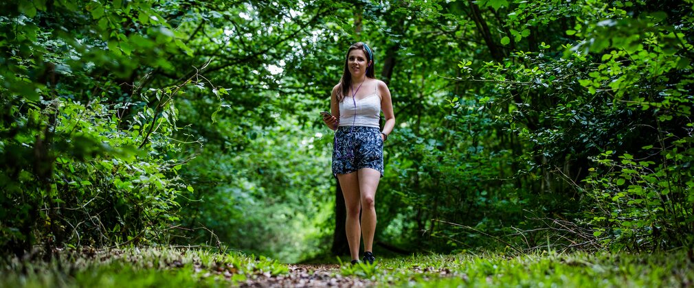 A woman walks along a path surrounded by green trees