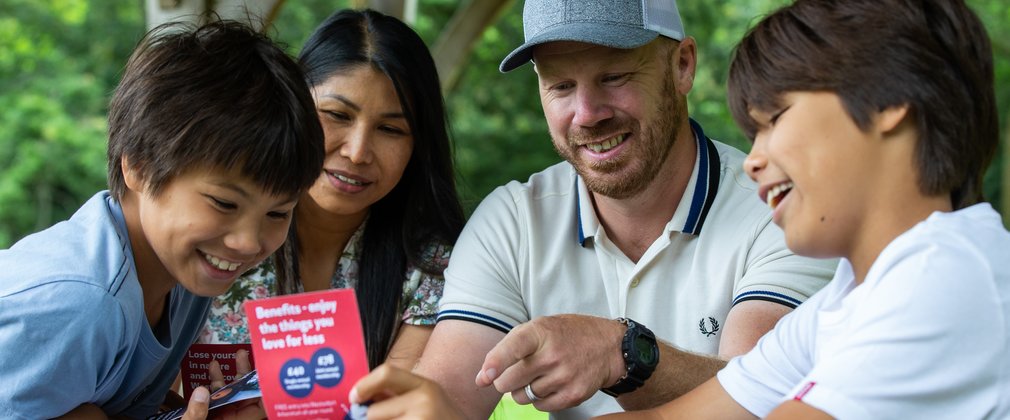 A Mum and Dad with their 2 young boys look joyfully at a Friends of Westonbirt Arboretum leaflet. 'Kids go free looks good!'