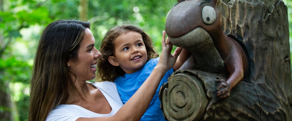 A woman holds her young daughter up to a sculpture of the squirrel from the gruffalo story