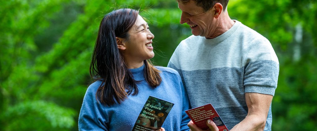 A husband and wife smile at each other holding a Friends of Westonbirt Arboretum leaflet in their hands