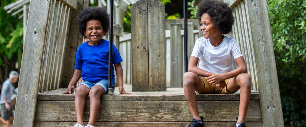 2 young boys sit on a wooden playing feature smiling to the camera