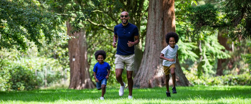 Man and two boys running on grass surrounded by trees