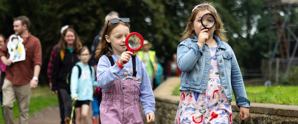 2 young girls walk holding magnifying glasses to their eyes.