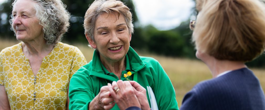 A volunteer in green holds a wildflower for a visitor to admire