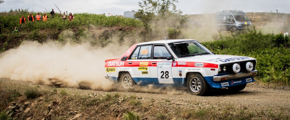 A white, blue and red rally car on a dirt track with dust billowing behind