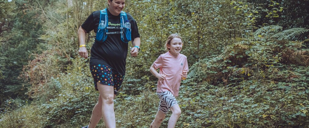 A person and a child running along a trail in the forest