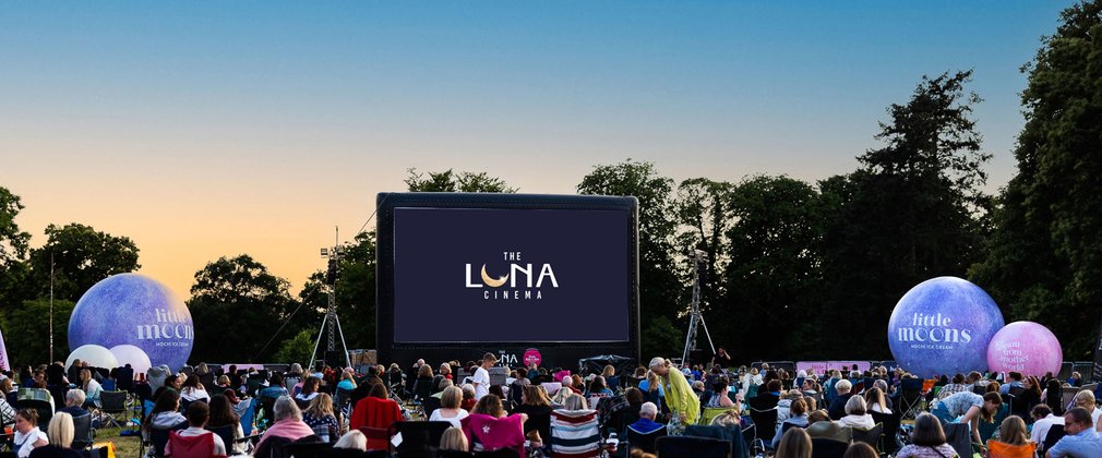 A crowd gather in the forest to watch an outdoor cinema screening at Westonbirt Arboretum