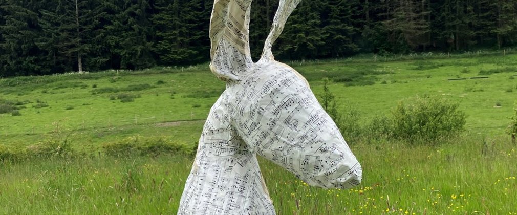 A sculpture of a hare made out of music sheets placed in the forest