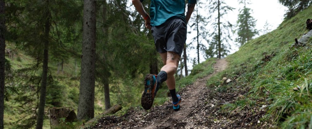 Man running on a small, hilly trail in the forest