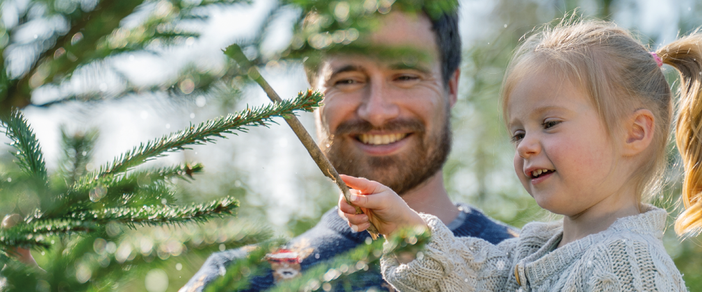 dad and young daughter smiling at a Christmas tree