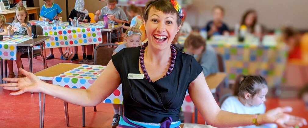 A photograph of a person leading a craft activity in a classroom full of children