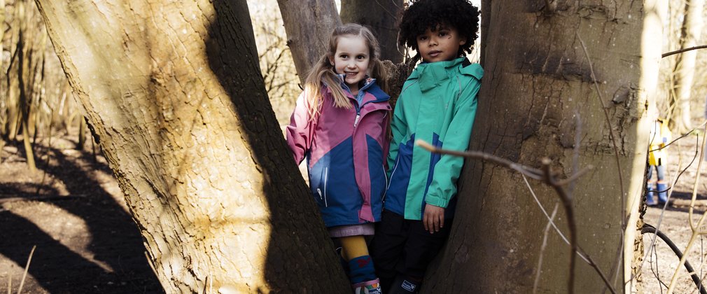 Two children in coats standing within a tree