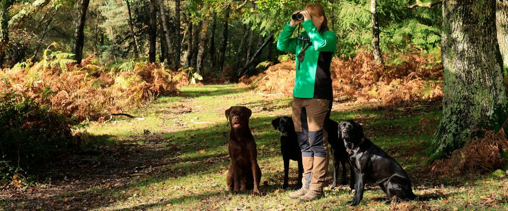A woman wearing Forestry England branded uniform standing with four and looking through binoculars.