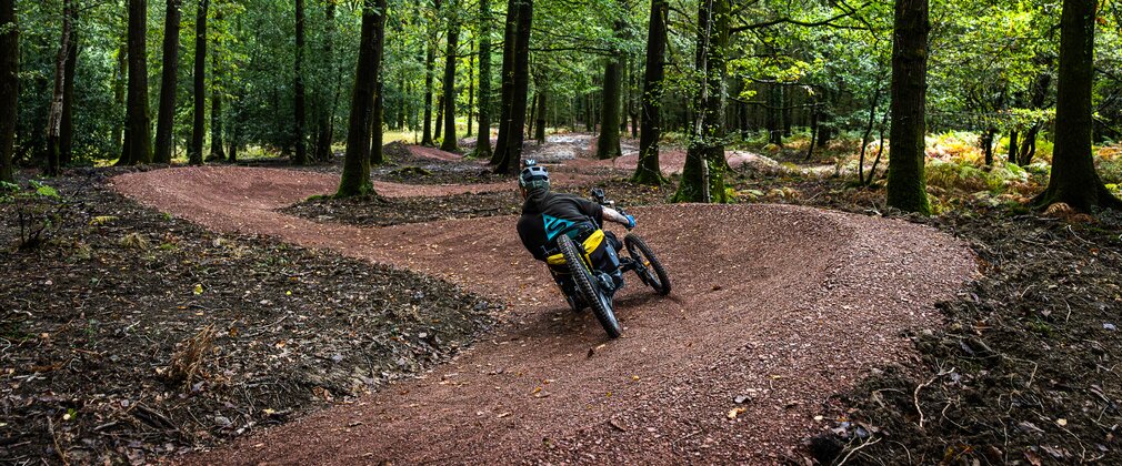 A man riding a three wheeled adapted bike along a mountain bike trail in a forest