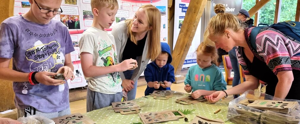 A family stand around a table of crafts. The adults help the children with the craft they are making