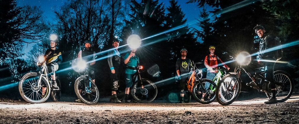 Mountain bikers in a line at night time with head torches shining.