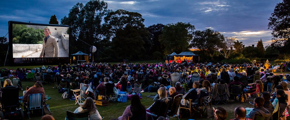 A crowd gather in the forest to watch an outdoor cinema screening of No Time To Die