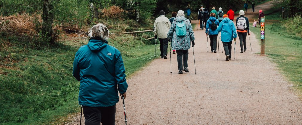 Over 50s nordic walking of gravel path in forest from behind