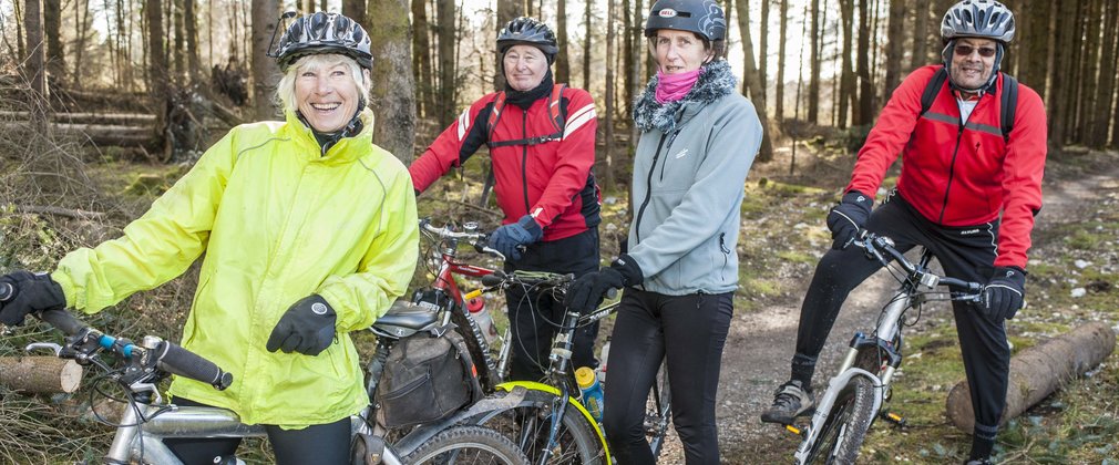 A group of smiling cyclists posing with bikes in the forest.