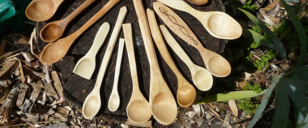 A variety of spoons carved out of wood are presented on a tree trunk log
