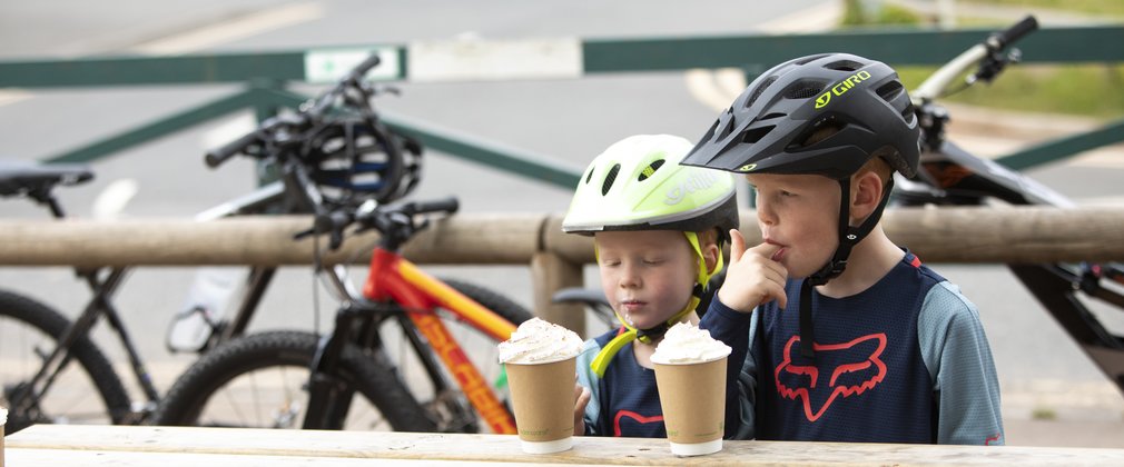 Two children enjoying a hot chocolate with bikes in the background