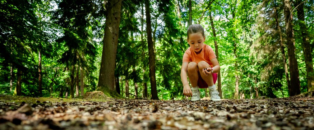 Young girl bent down on a path in the forest looking at something in her handd