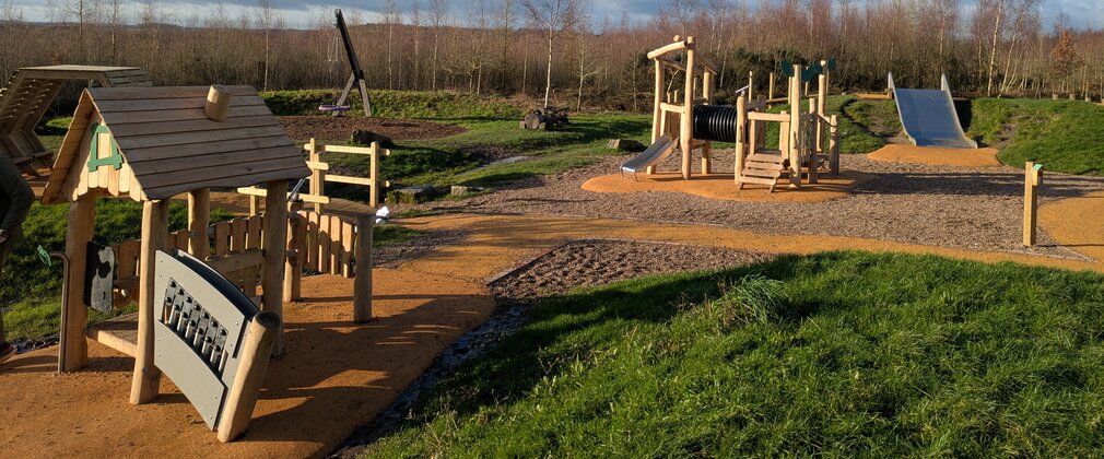 Timber play equipment plus metal slides and a tyre swing in the background