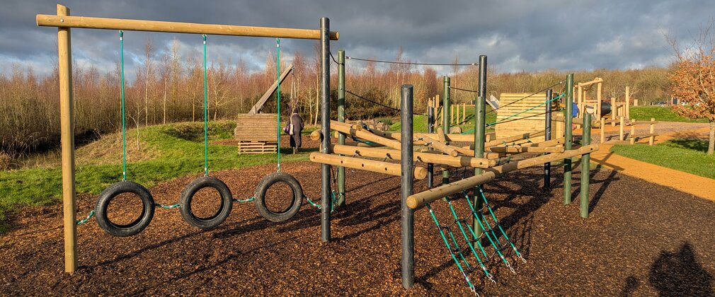 Timber play equipment featuring climbing net and hanging tyres