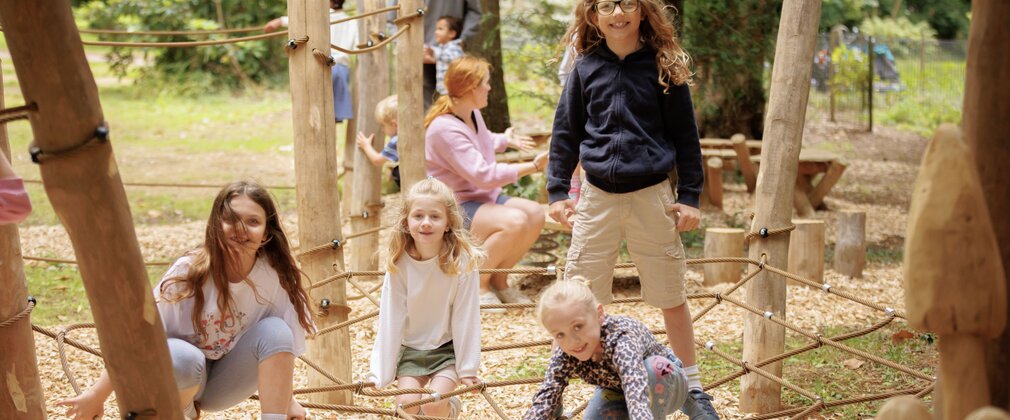 Kids play in the playground on a spider web rope feature. 